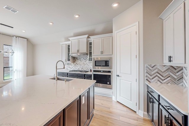 kitchen with tasteful backsplash, white cabinets, appliances with stainless steel finishes, light hardwood / wood-style floors, and sink