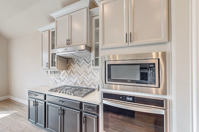 kitchen featuring backsplash, gray cabinetry, white cabinetry, appliances with stainless steel finishes, and light hardwood / wood-style floors