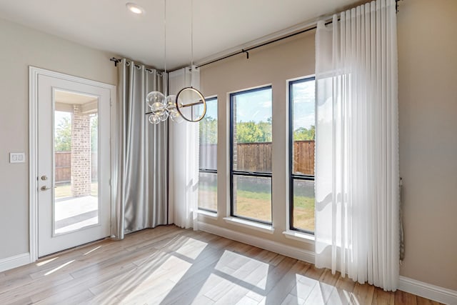 doorway featuring light wood-type flooring, an inviting chandelier, and plenty of natural light