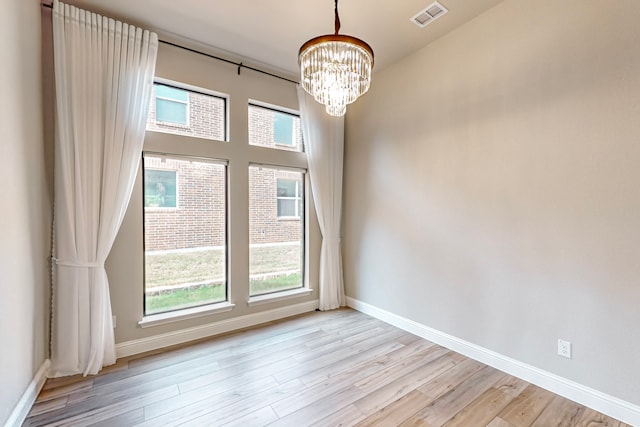 empty room featuring a chandelier and light wood-type flooring