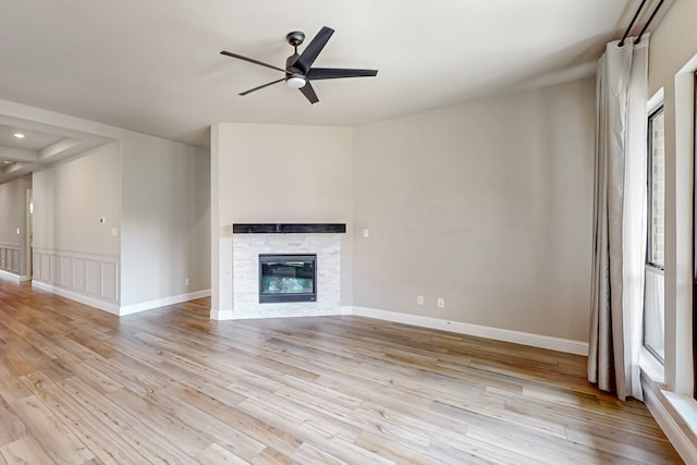 unfurnished living room featuring ceiling fan, light wood-type flooring, a wealth of natural light, and a stone fireplace