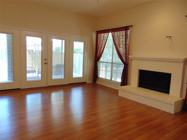 unfurnished living room featuring hardwood / wood-style flooring, a brick fireplace, and french doors