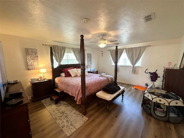 bedroom with a ceiling fan, a textured ceiling, dark wood finished floors, baseboards, and visible vents