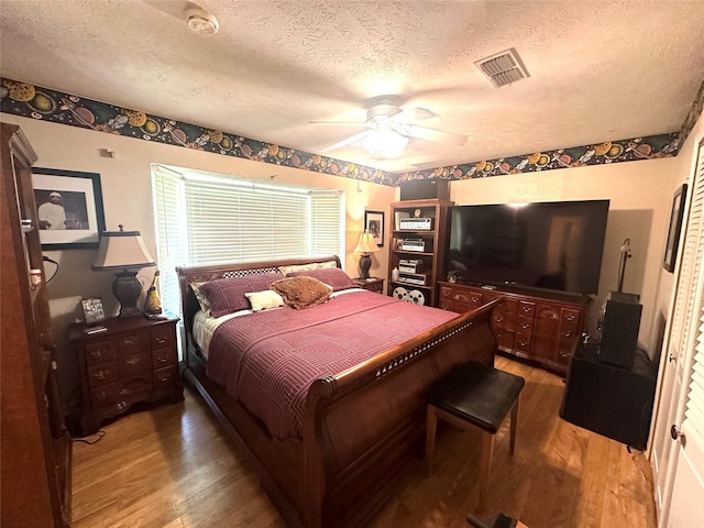 bedroom featuring ceiling fan, hardwood / wood-style floors, visible vents, and a textured ceiling