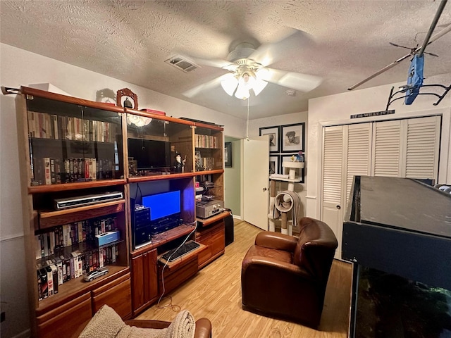 living room featuring ceiling fan, a textured ceiling, visible vents, and light wood-style flooring