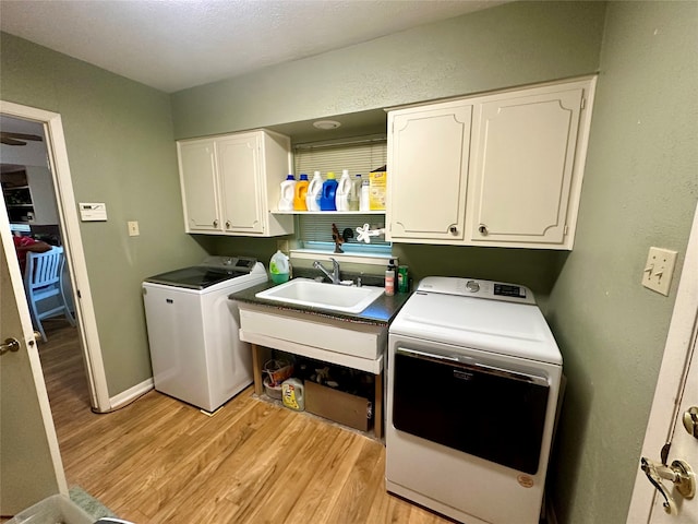 clothes washing area featuring washing machine and dryer, sink, cabinets, and light wood-type flooring