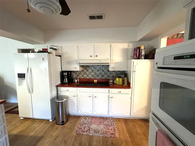 kitchen with dark countertops, white appliances, white cabinetry, under cabinet range hood, and visible vents