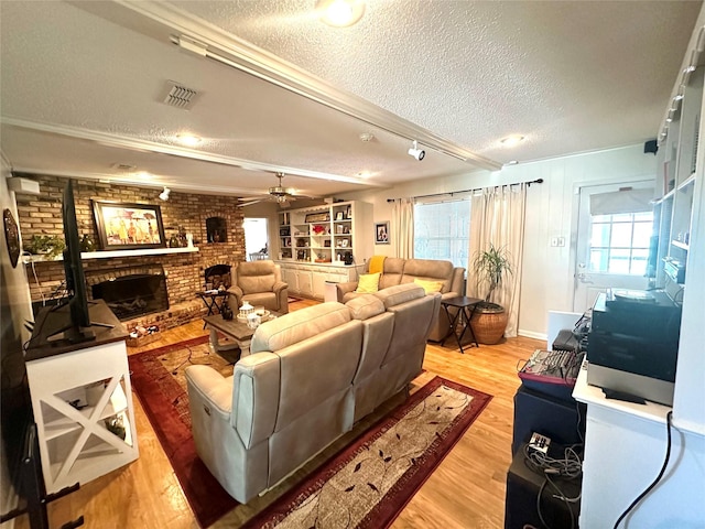 living area with visible vents, a brick fireplace, light wood-style floors, and a textured ceiling