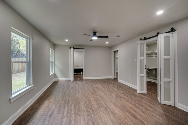 interior space featuring connected bathroom, dark hardwood / wood-style floors, ceiling fan, and a barn door