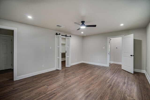 unfurnished bedroom featuring dark wood-type flooring, a spacious closet, ceiling fan, and a barn door