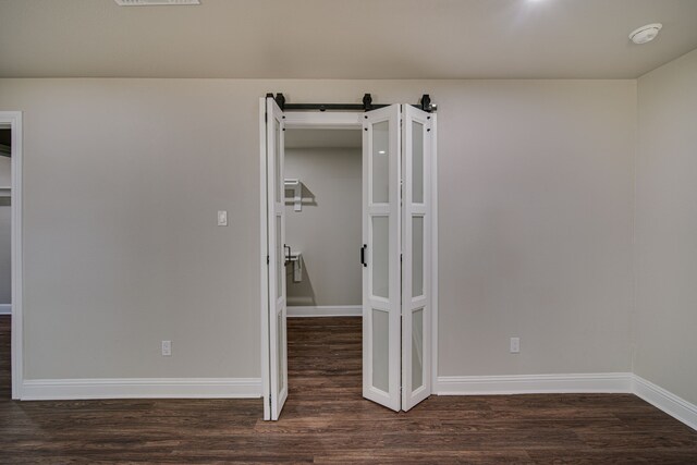 unfurnished bedroom with a barn door and dark hardwood / wood-style floors