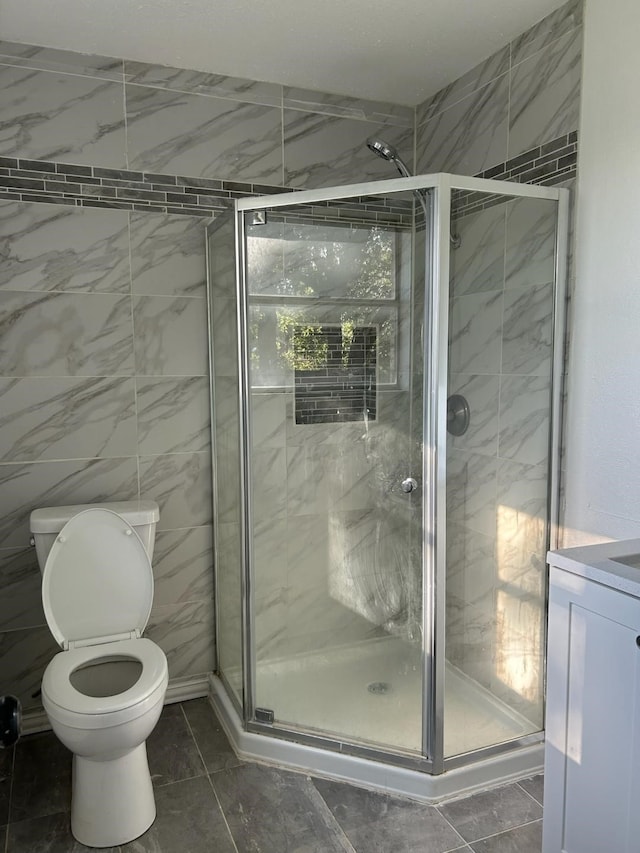 bathroom with tile patterned floors, vanity, tile walls, toilet, and walk in shower