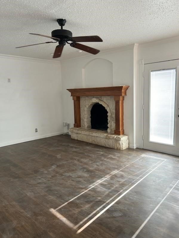 unfurnished living room featuring a stone fireplace, ornamental molding, wood-type flooring, a textured ceiling, and ceiling fan