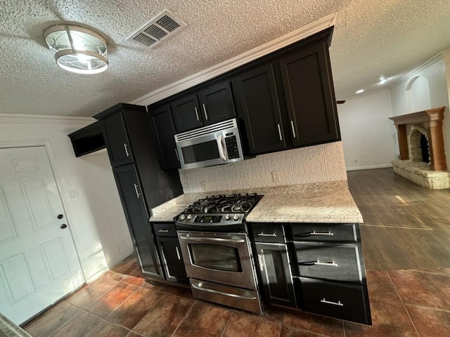 kitchen with appliances with stainless steel finishes, crown molding, a textured ceiling, and backsplash