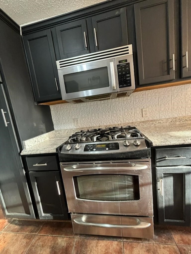 kitchen with appliances with stainless steel finishes, decorative backsplash, a textured ceiling, and dark tile patterned floors