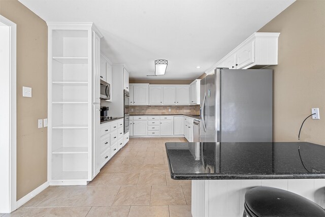 kitchen with stainless steel appliances, decorative backsplash, white cabinetry, a kitchen bar, and light tile patterned floors