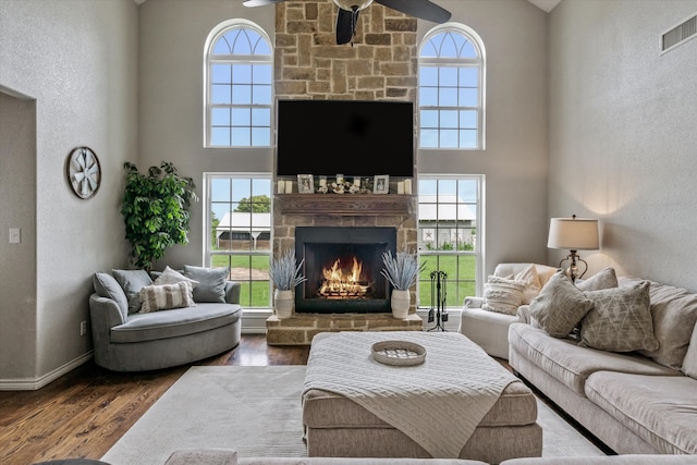 living room featuring a towering ceiling, ceiling fan, a stone fireplace, and wood-type flooring