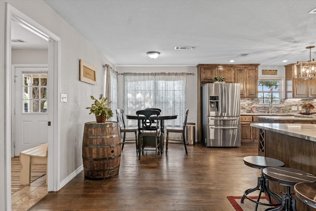 kitchen featuring dark hardwood / wood-style floors, tasteful backsplash, light stone countertops, pendant lighting, and stainless steel fridge with ice dispenser