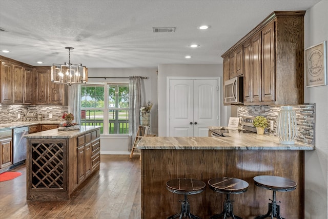 kitchen featuring a kitchen bar, dark hardwood / wood-style flooring, appliances with stainless steel finishes, decorative backsplash, and light stone countertops