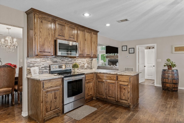 kitchen with appliances with stainless steel finishes, dark hardwood / wood-style floors, tasteful backsplash, kitchen peninsula, and a notable chandelier