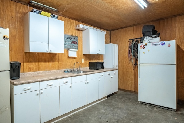 kitchen with sink, wooden walls, white refrigerator, and white cabinetry