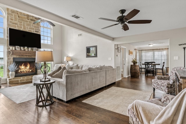 living room featuring a stone fireplace, ceiling fan, and dark hardwood / wood-style flooring