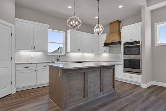 kitchen with a kitchen island, stainless steel double oven, a chandelier, white cabinetry, and custom exhaust hood