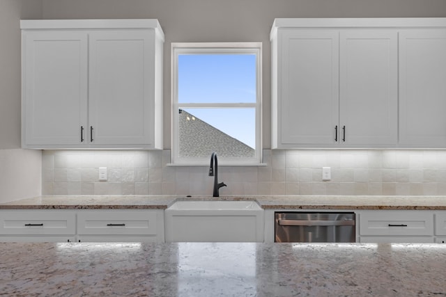 kitchen featuring stainless steel dishwasher, light stone counters, and white cabinets