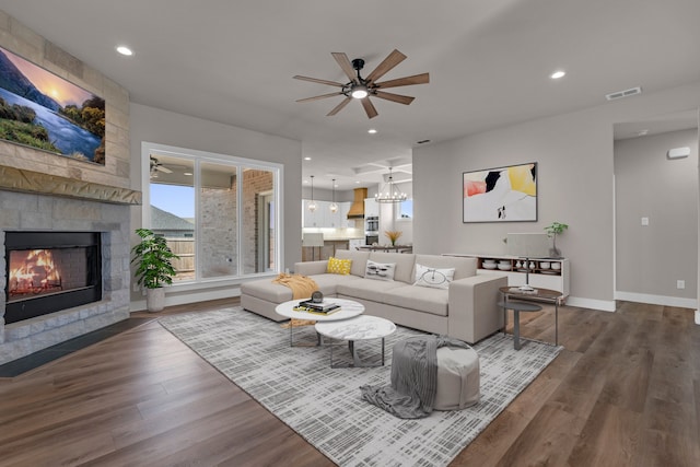 living room featuring ceiling fan with notable chandelier, dark hardwood / wood-style floors, and a tile fireplace