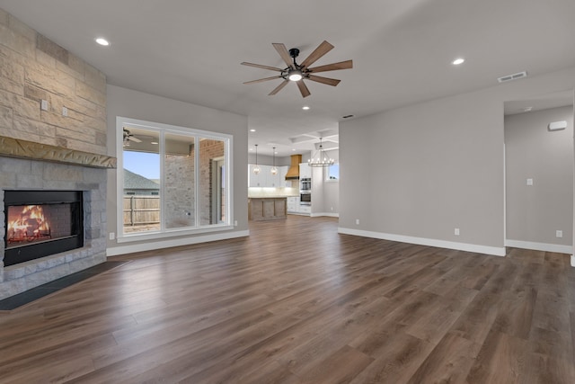 unfurnished living room featuring ceiling fan with notable chandelier, dark hardwood / wood-style flooring, and a fireplace