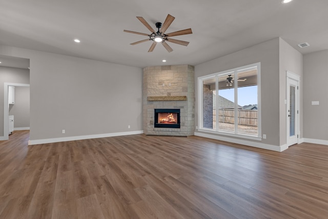 unfurnished living room featuring ceiling fan, a stone fireplace, and wood-type flooring