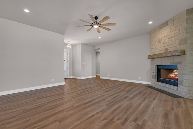 unfurnished living room with hardwood / wood-style floors, ceiling fan, and a stone fireplace