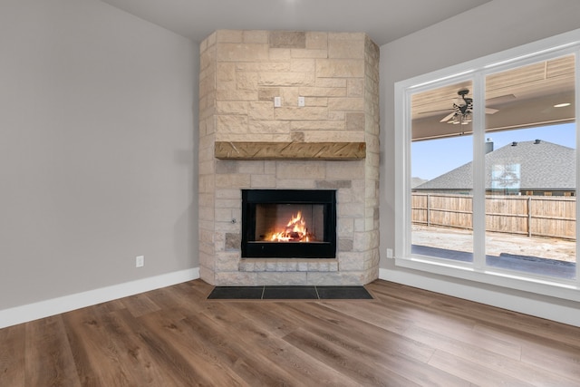 unfurnished living room featuring hardwood / wood-style floors, ceiling fan, and a stone fireplace