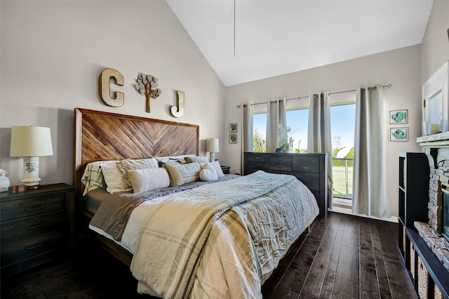 bedroom with dark hardwood / wood-style flooring, a stone fireplace, and high vaulted ceiling