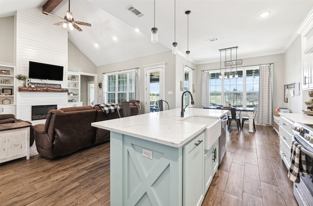 kitchen featuring hanging light fixtures, ceiling fan with notable chandelier, light stone countertops, dark wood-type flooring, and a center island with sink