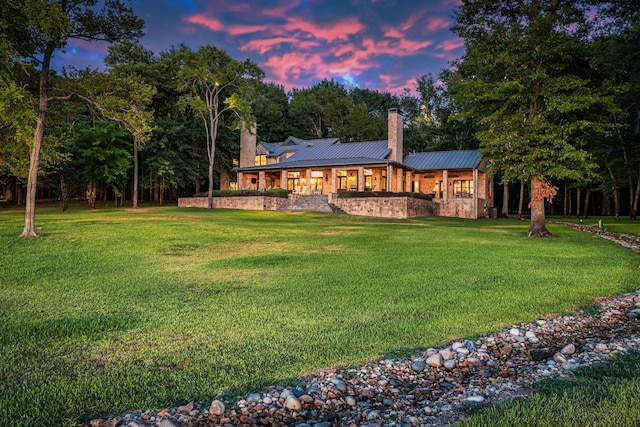 back house at dusk featuring a lawn