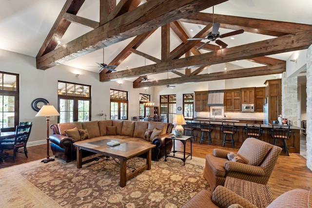 living room with ceiling fan, high vaulted ceiling, beamed ceiling, and light wood-type flooring