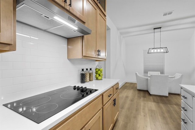 kitchen with tasteful backsplash, pendant lighting, black electric stovetop, and light hardwood / wood-style flooring