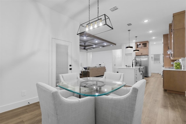 dining room with light wood-type flooring, coffered ceiling, and ceiling fan