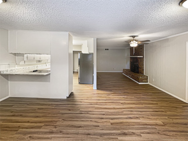 kitchen featuring white cabinetry, stainless steel refrigerator, a fireplace, a textured ceiling, and wood-type flooring