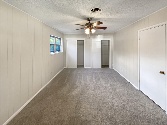 unfurnished bedroom with ceiling fan, carpet flooring, a textured ceiling, and multiple closets