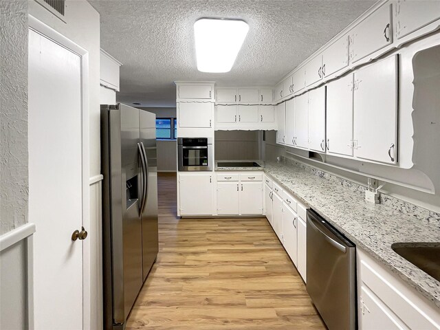 kitchen with white cabinetry, appliances with stainless steel finishes, light stone countertops, light hardwood / wood-style floors, and a textured ceiling