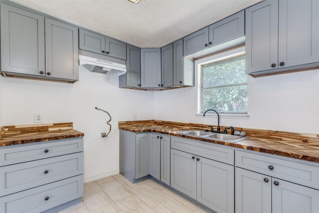 kitchen featuring sink, butcher block counters, light tile patterned floors, and gray cabinetry