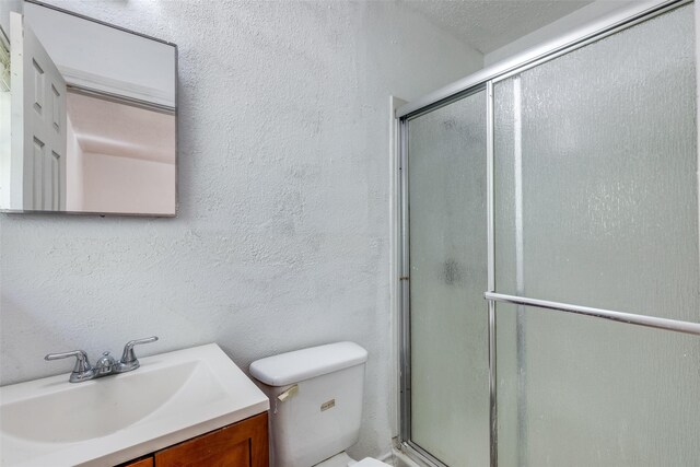 bathroom featuring a shower with shower door, toilet, a textured ceiling, and vanity