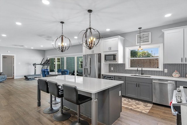 kitchen featuring backsplash, sink, hanging light fixtures, wood-type flooring, and stainless steel appliances