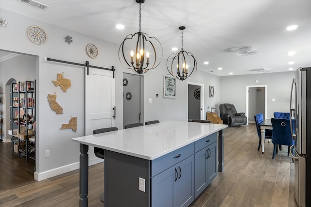 kitchen with stainless steel fridge, dark hardwood / wood-style flooring, a breakfast bar area, a barn door, and pendant lighting