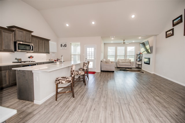 kitchen featuring ceiling fan, light hardwood / wood-style flooring, high vaulted ceiling, a center island, and dark brown cabinets