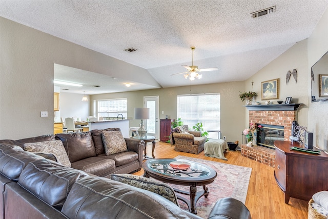 living room featuring ceiling fan, light hardwood / wood-style floors, a brick fireplace, and lofted ceiling