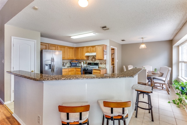 kitchen featuring backsplash, appliances with stainless steel finishes, decorative light fixtures, a textured ceiling, and light tile patterned flooring