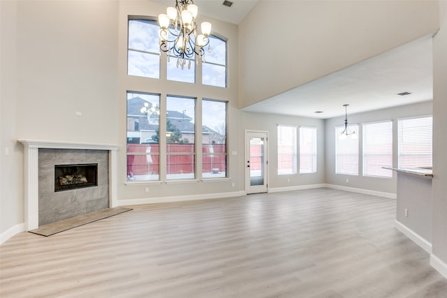 unfurnished living room featuring a towering ceiling, light hardwood / wood-style flooring, a chandelier, and a premium fireplace